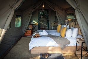 Alojamiento con carpa que incluye una cama, almohadas, una lámpara y una mesita.