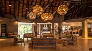A spacious lobby with a high ceiling, wooden beams, and a central seating area with sofas and a bench. There are signs for 'Departures' and 'Arrivals' indicating a transportation hub. - Kruger Untamed - Tshokwane River Camp (Skukuza)