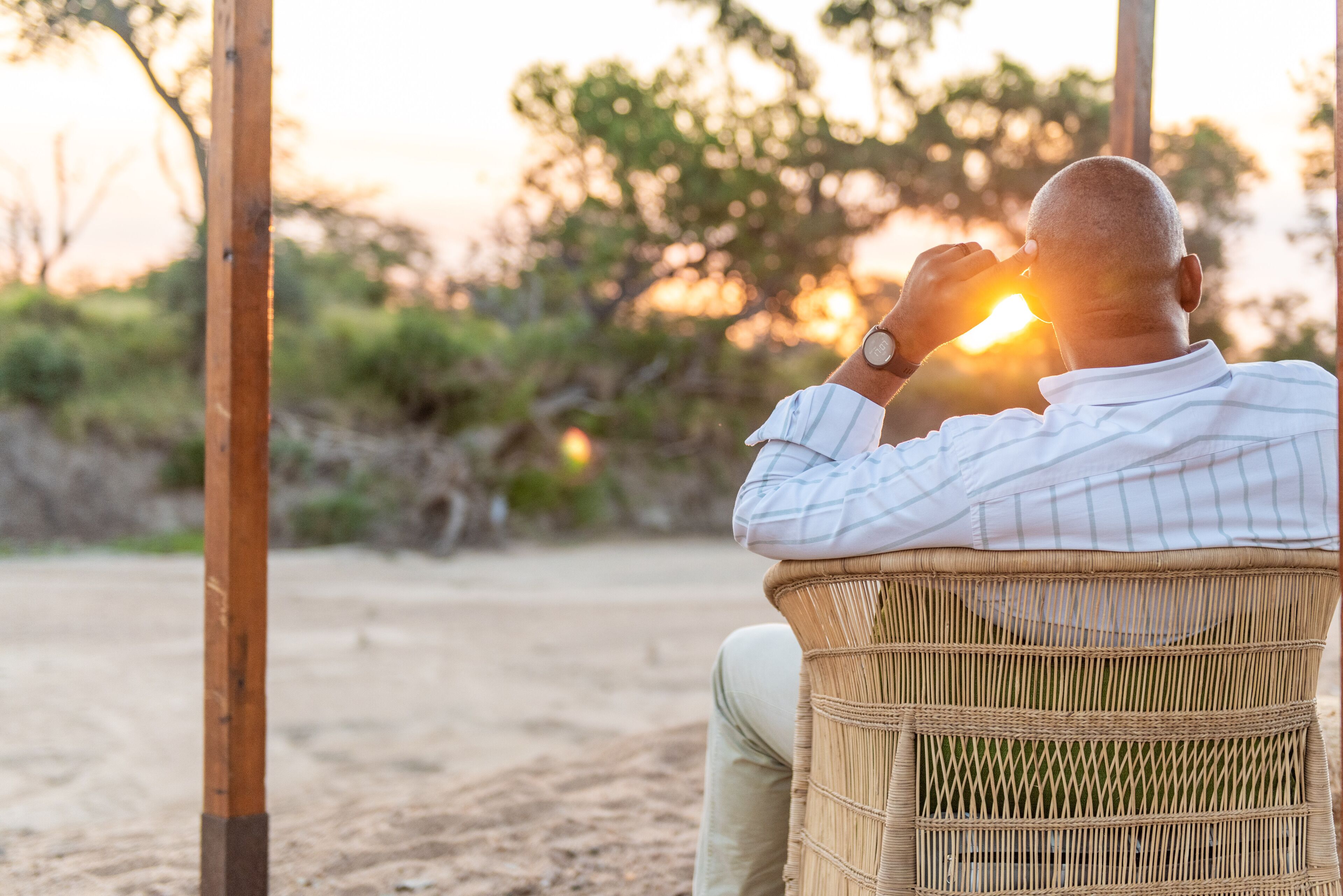 A person sitting on a wicker chair outdoors during sunset.