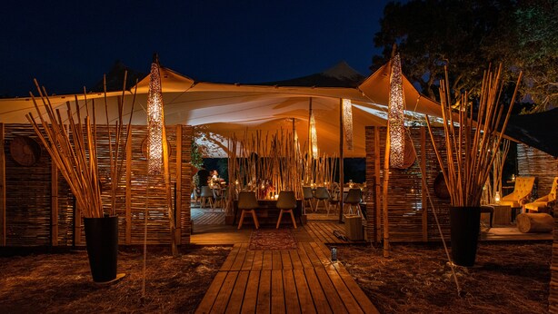 A tented outdoor dining area with bamboo decorations, a wooden deck, and a view of a mountain in the background. - Kruger Untamed - Tshokwane River Camp (Skukuza)