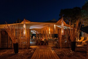 A tented outdoor dining area with bamboo decorations, a wooden deck, and a view of a mountain in the background. - Kruger Untamed - Tshokwane River Camp (Skukuza)