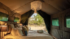 Una tienda de campaña con cama, almohadas, una lámpara y vistas al exterior.