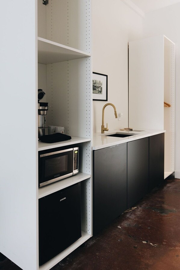 A modern kitchen with white cabinetry, a stainless steel microwave, and a gold faucet.