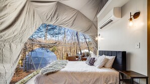 A tented room with a bed, a chair, a table, and a wall-mounted light fixture.