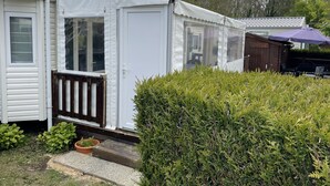 A mobile home with a white exterior, a wooden deck, and a covered porch area. - Charmant Mobile-home Cosy (Bernières-sur-Mer)