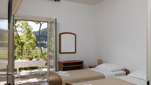 A hotel room with two beds, a small table with a basket of fruit, a mirror on the wall, and a view of greenery and hills outside. - Begovic Guest House - Private Twin Room (Dubrovnik)
