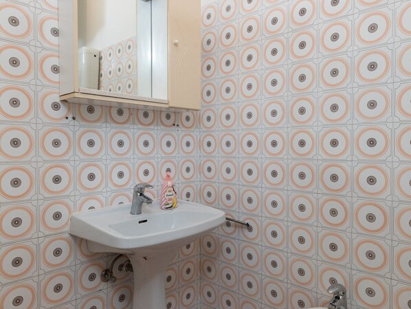 A bathroom with a sink, mirror, and patterned wall tiles.
