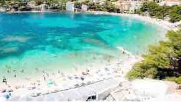 A coastal beach scene with clear turquoise water, sandy shore, and some greenery. - Superbe Appartement Cosy à 300 m de la Plage (Bandol)