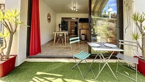 A patio with a dining table and chairs, a red curtain, and potted plants. - Superbe Appartement Cosy à 300 m de la Plage (Bandol)