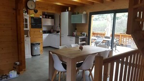 A wooden cabin interior with a dining area, kitchen, and a balcony with a view. - Chalet au Calme, vue Magnifique (Glières-Val-de-Borne)