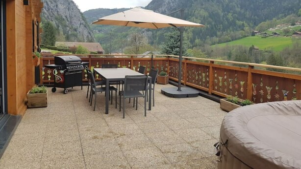 A wooden deck with a table and chairs, a barbecue grill, and a view of a mountainous landscape. - Chalet au Calme, vue Magnifique (Glières-Val-de-Borne)