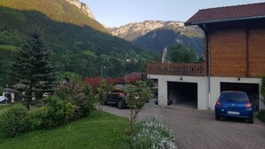 A building with a garage, surrounded by greenery and mountains. - Chalet au Calme, vue Magnifique (Glières-Val-de-Borne)