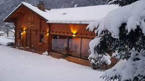 A wooden cabin with a snow-covered roof, large windows, and a warm interior light. - Chalet au Calme, vue Magnifique (Glières-Val-de-Borne)