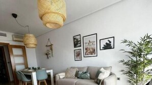 Ein modernes Wohnzimmer mit Sofa, Sesseln, einem Esstisch und einer Pendelleuchte.