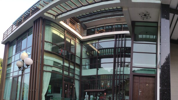 A modern building with large glass windows, a curved facade, and a small outdoor area with steps leading to a door. - Seth Spring B&B (Datong)