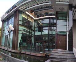 Un edificio moderno con amplios ventanales, fachada curva y un pequeño espacio exterior con escalones que conducen a una puerta.