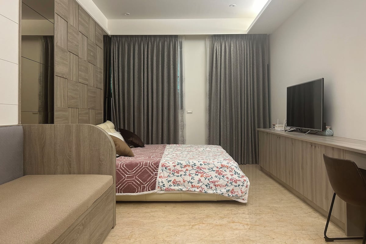 Un dormitorio moderno con cama, televisor y escritorio.