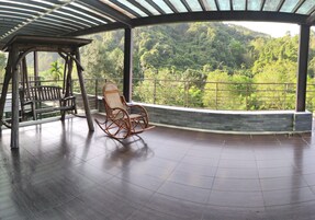 Un espacio al aire libre techado con una silla colgante de madera y una mecedora de madera.