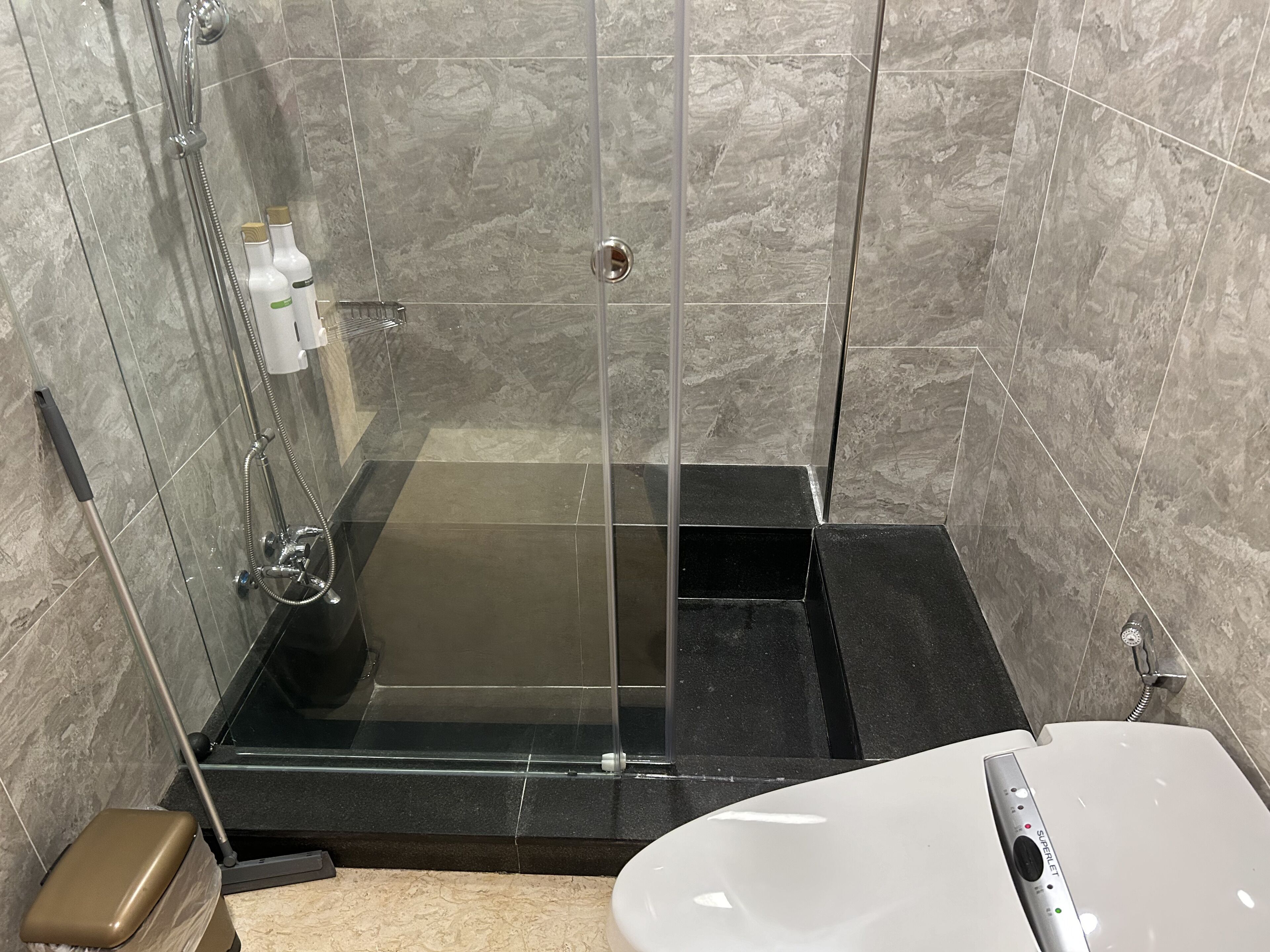 Un baño moderno con ducha envuelta en vidrio, una bañera negra y un lavamanos blanco con grifo.