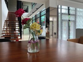 Una sala de estar moderna con una escalera de madera, un florero con flores sobre una mesa y ventanas amplias.