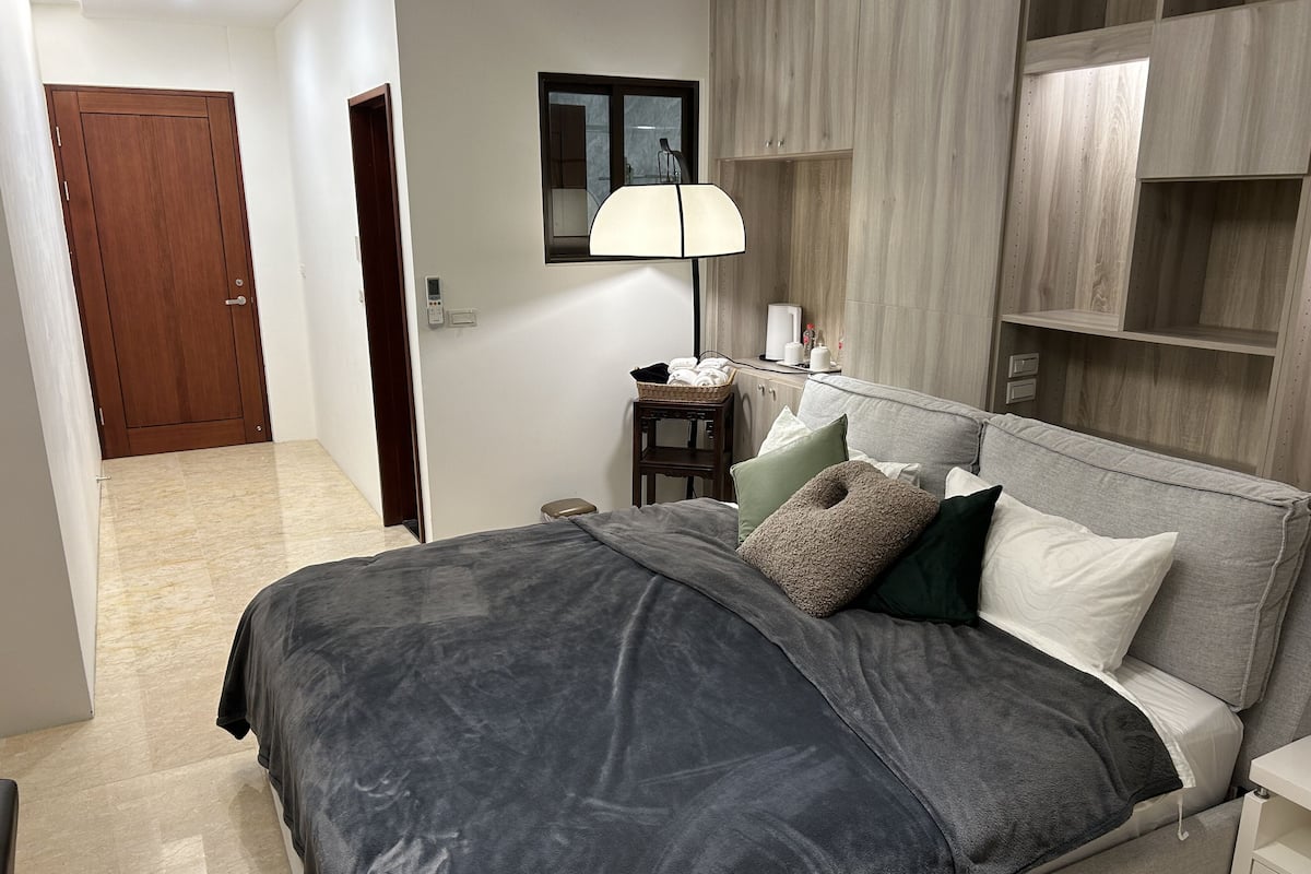 Un dormitorio moderno con cama, mesita de noche, lámpara y armario de madera.