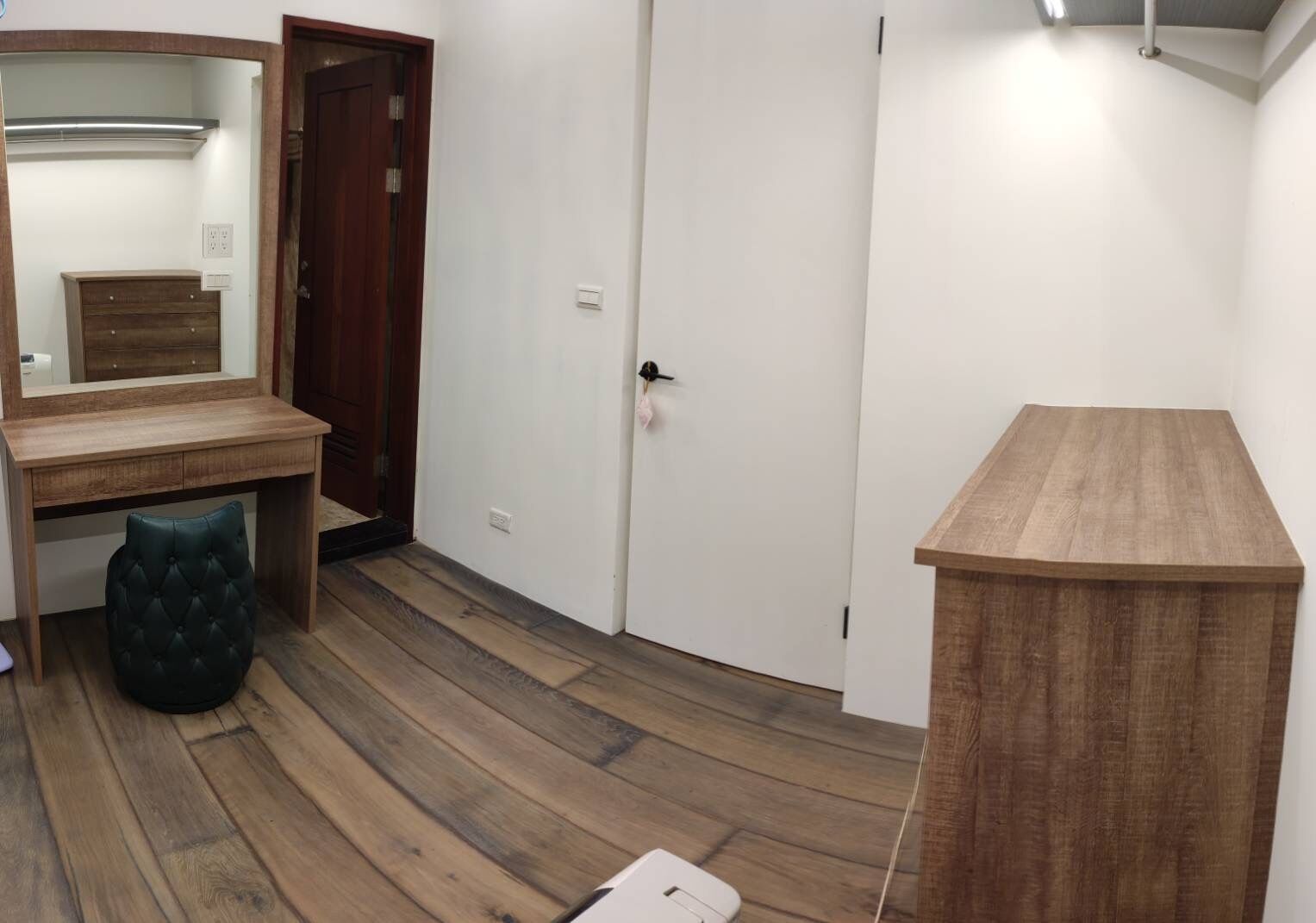 A room with a wooden desk, a chair, a wardrobe, and a bedside table.