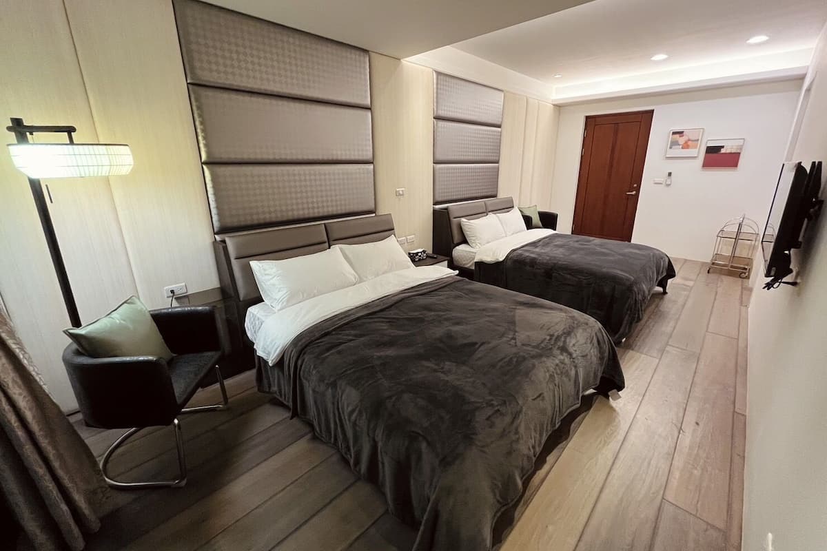 Habitación de hotel con dos camas, un escritorio, una silla, un televisor y una puerta.