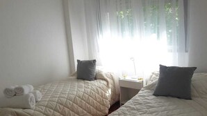 A hotel room with two beds, each with a quilted bedspread and pillows. There are towels on the beds and a nightstand with a lamp between the beds.