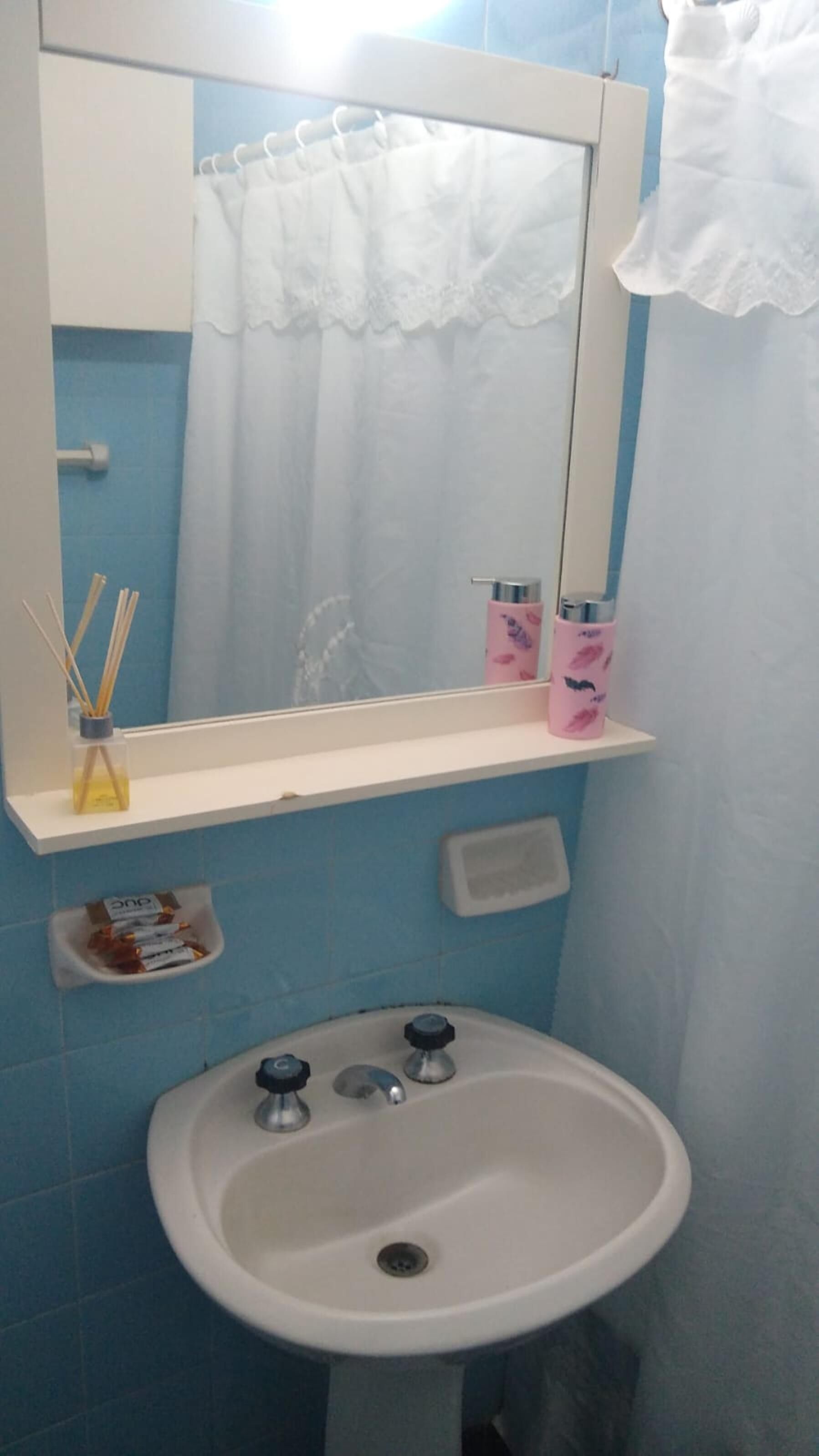 A bathroom with a white sink, a mirror, and a shelf with personal care items.