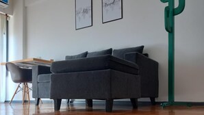 A modern living room with a grey sofa, wooden flooring, and two framed wall art pieces. - Beautiful Apartment in Av Boedo (Buenos Aires)