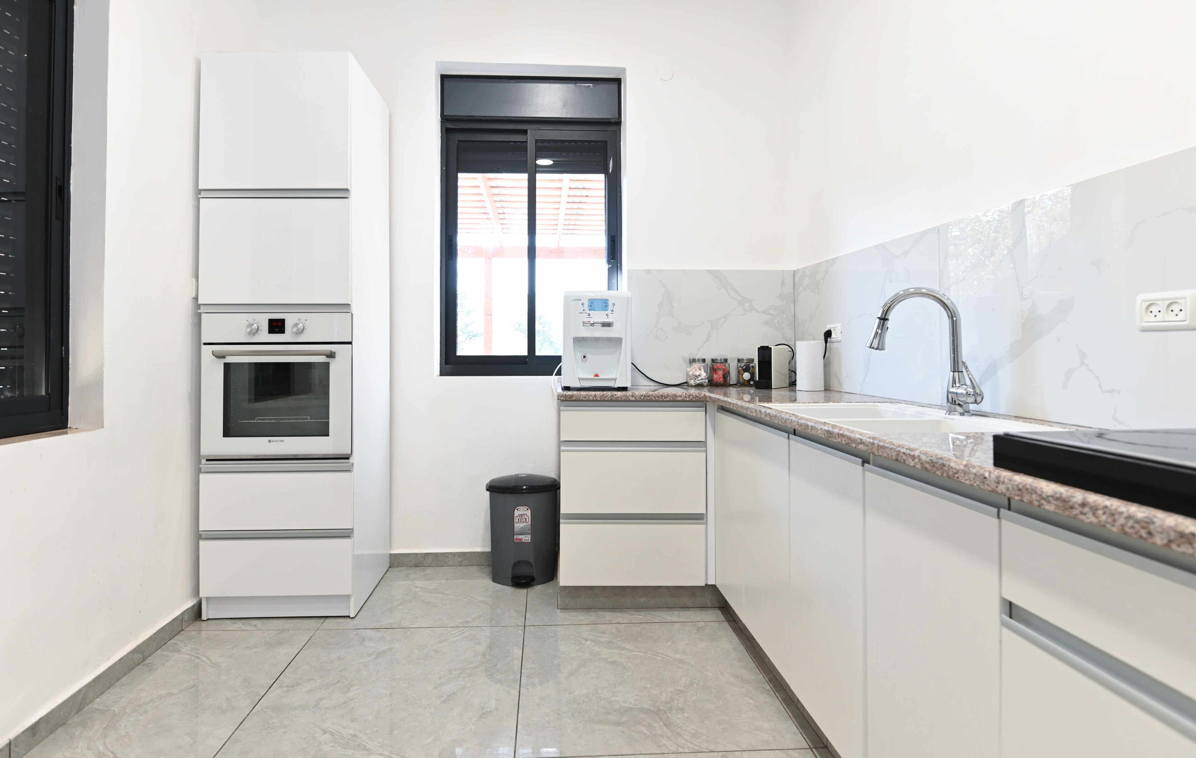 A modern kitchen with white cabinetry, a built-in oven, a water dispenser, and a sink with a faucet.