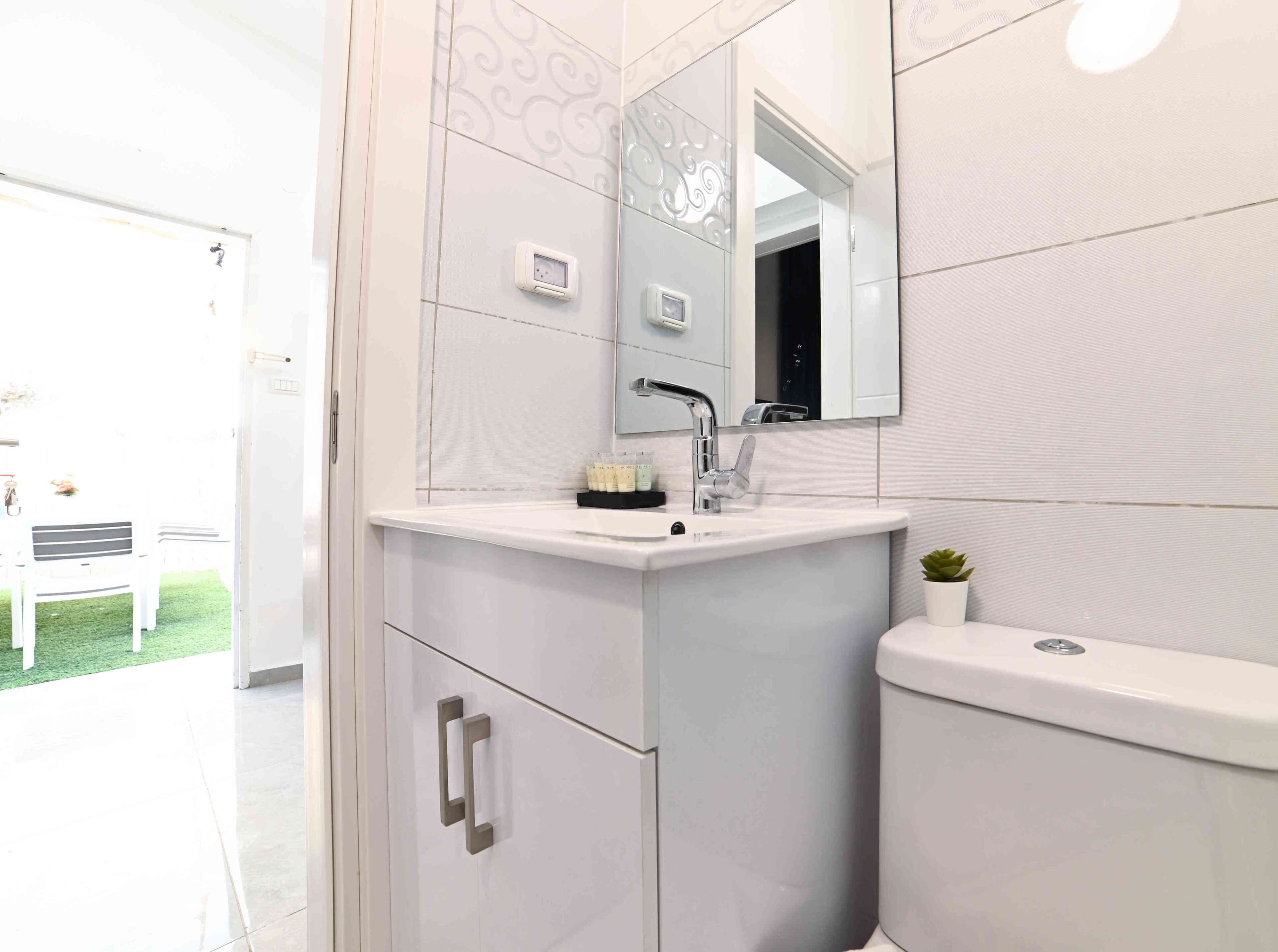 Un bagno moderno con un mobile lavabo bianco, un lavandino, uno specchio e un water.