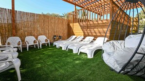 A covered outdoor seating area with white plastic chairs and lounge chairs, a wooden pergola, and a wooden fence in the background. - Yalarent Villa Viviana with private pool (Migdal)