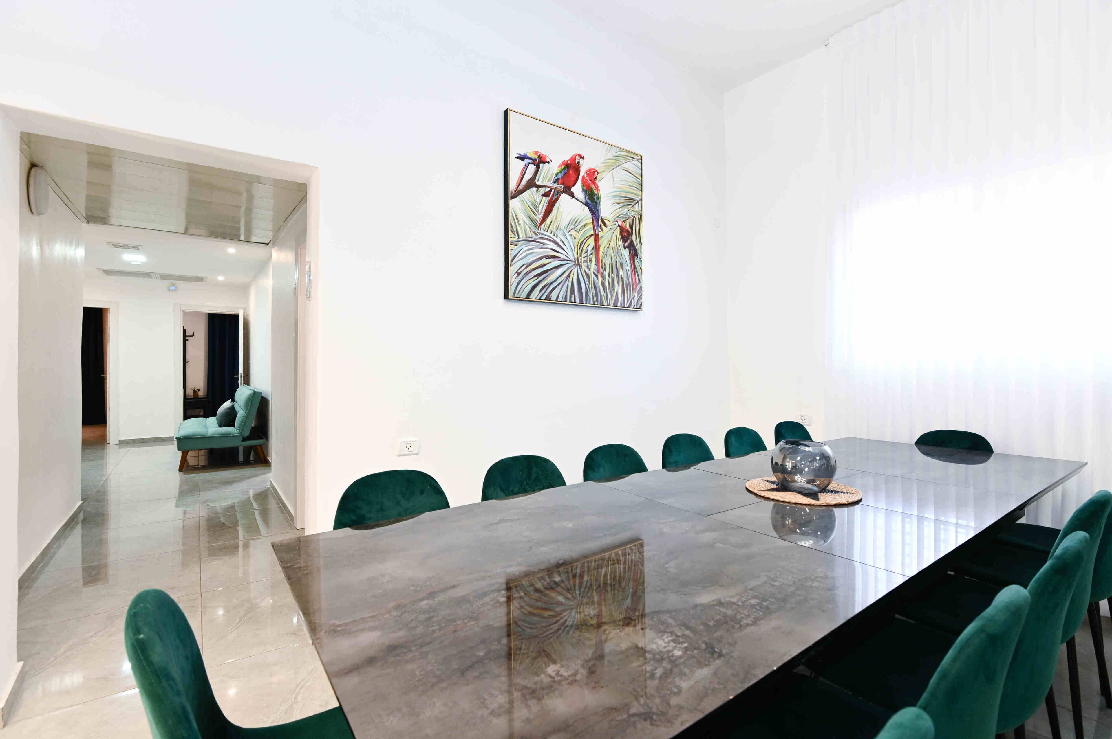 A conference room with a long table, green chairs, and a painting of parrots.