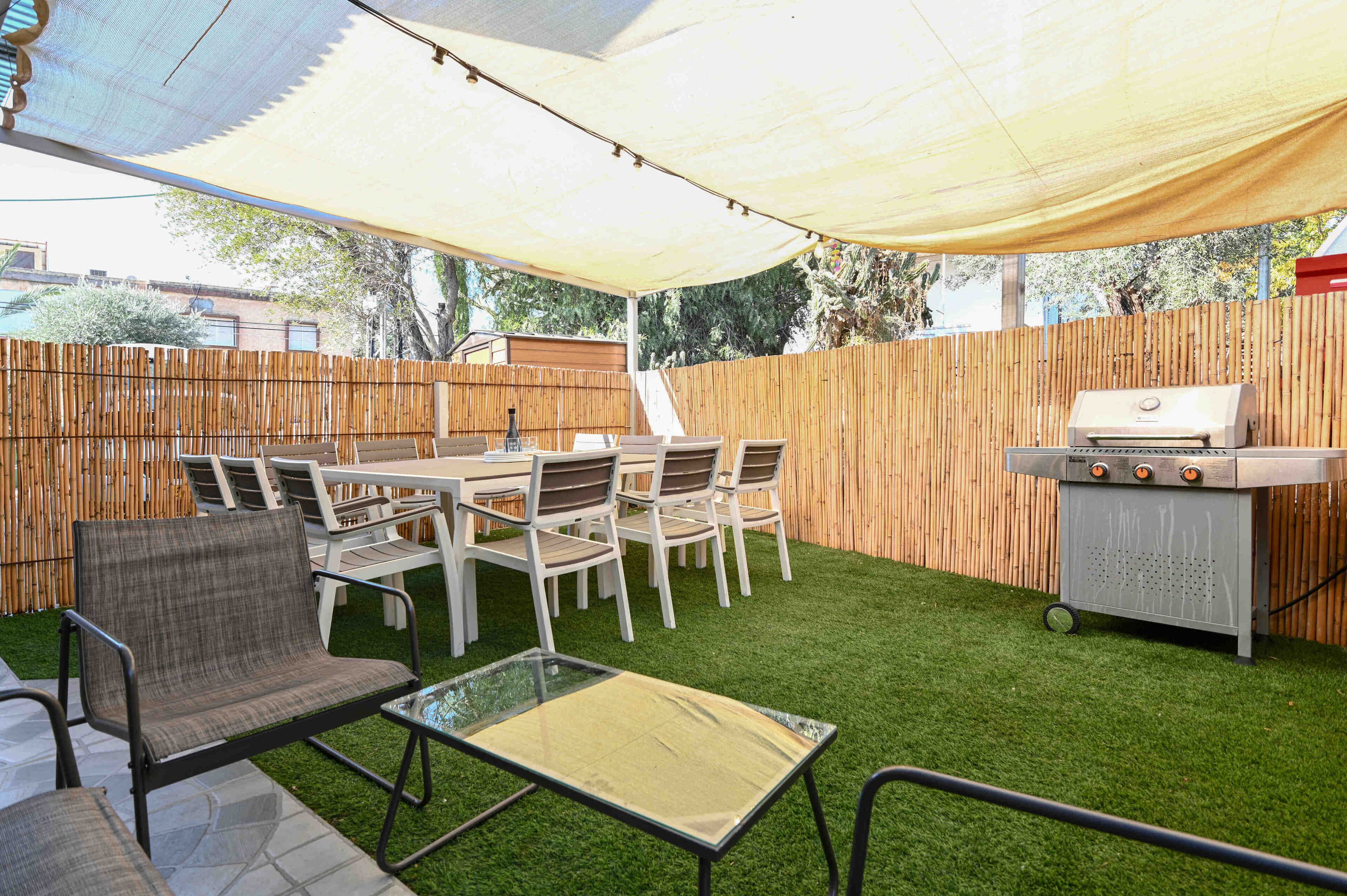 An outdoor patio with a table and chairs, a grill, and a bamboo fence.