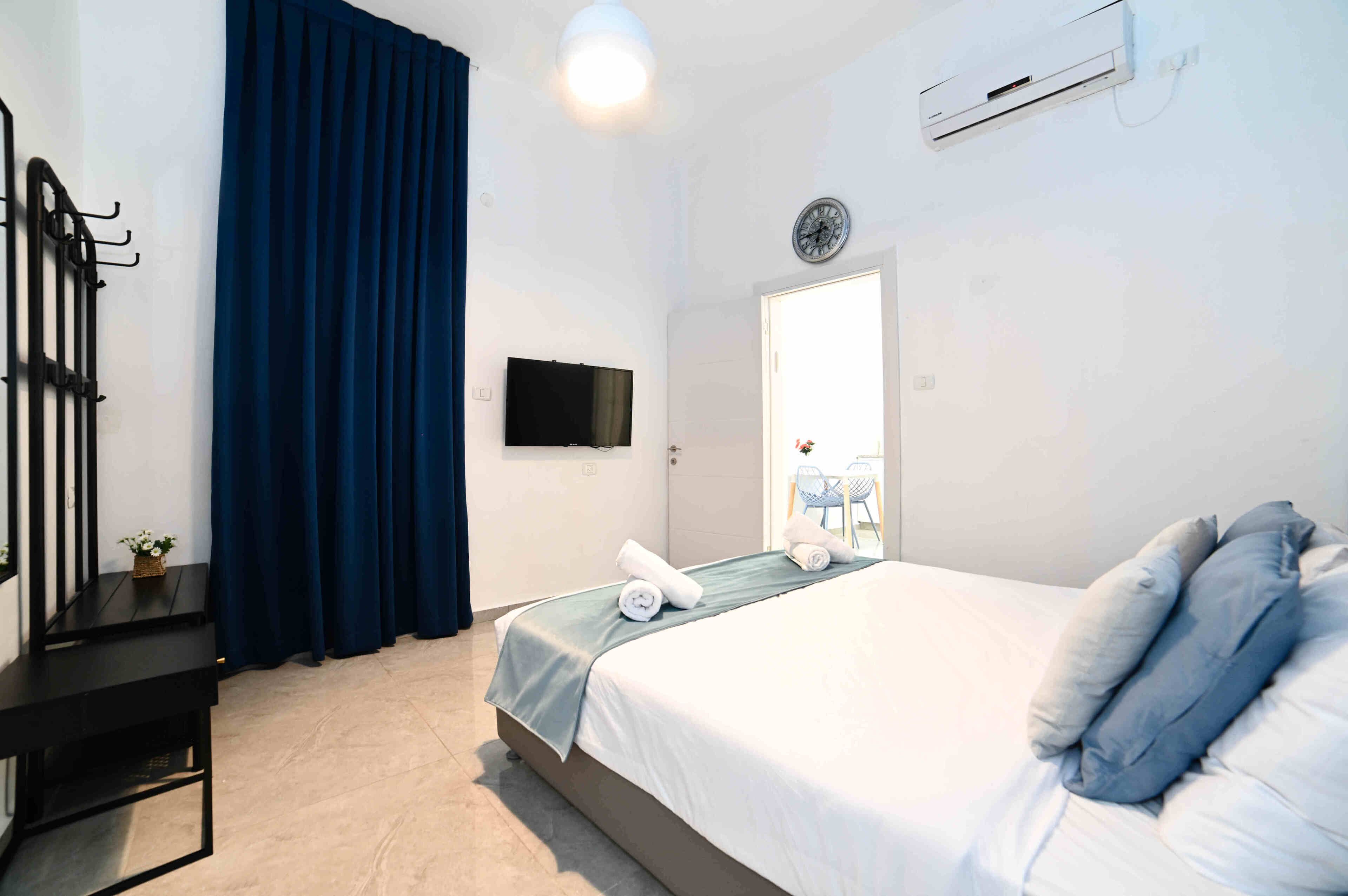 Una habitación de hotel con cama, televisión, reloj y aire acondicionado.