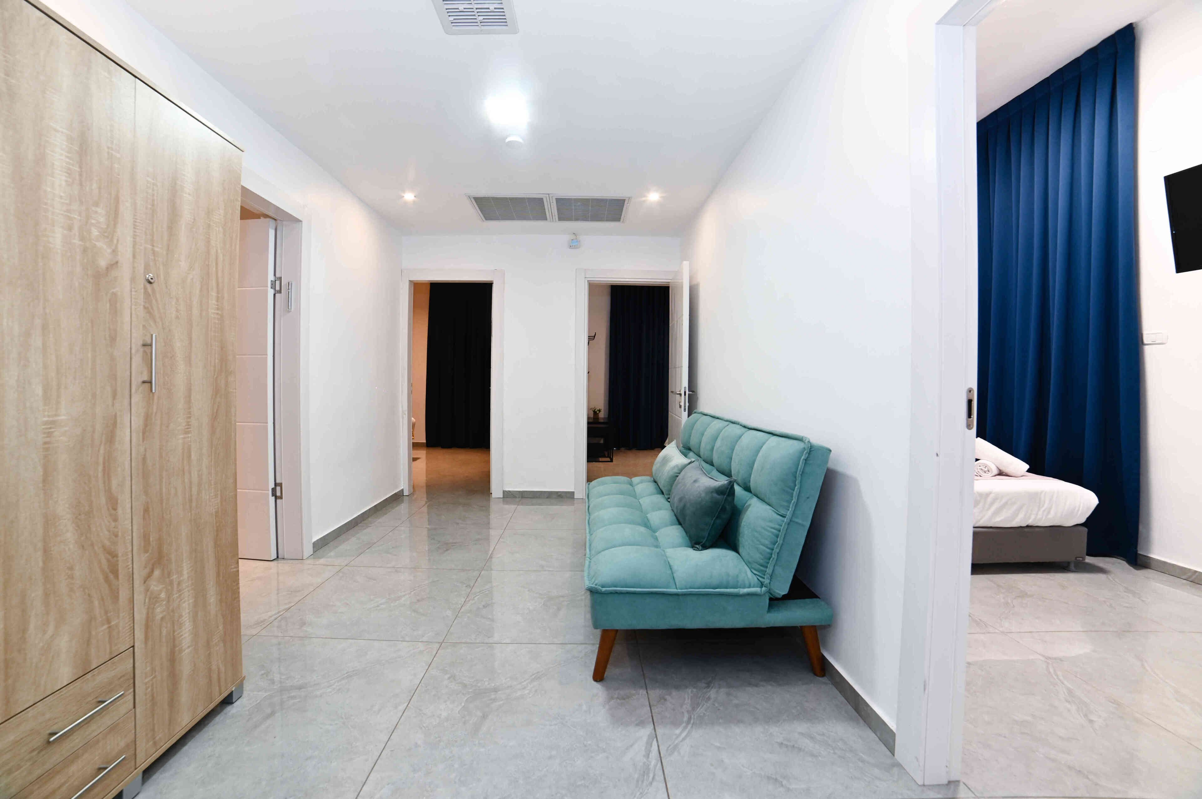 Een moderne hotelkamer met een blauwgroene bank, een houten garderobe en een bed met blauwe gordijnen.