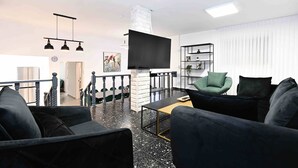 A modern living room with a flat-screen TV, black sofas, a green armchair, a marble floor, and a staircase leading to another room. - Yalarent Villa Viviana with private pool (Migdal)