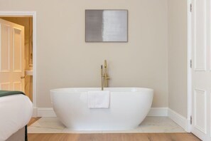 A modern bathroom with a freestanding bathtub, a towel, and a minimalist wall art piece.