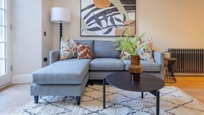 Ein modernes Wohnzimmer mit einer grauen Eckcouch, einem runden Couchtisch, einer Stehlampe und einem großen abstrakten Gemälde an der Wand.