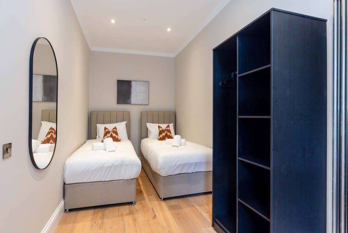 A bedroom with two beds, a large mirror, a wardrobe, and a painting on the wall.