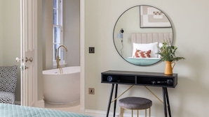 A bedroom with a bed, a bedside table with a lamp, a mirror, and a potted plant. - Jade Suite - City Centre 2 Bed Luxury Apartment (Edinburgh)