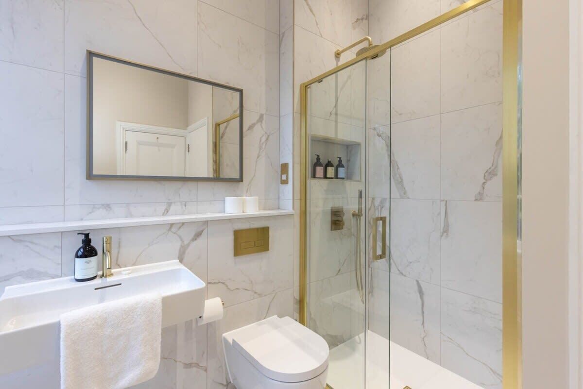 Een badkamer met een marmeren wastafel, een wit toilet, een douche met glazen wanden en een spiegel boven de wastafel.