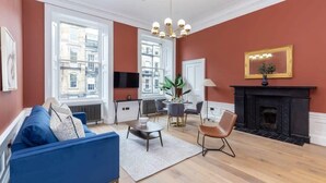 A living room with a blue sofa, a fireplace, a dining table with chairs, and large windows. - Ember Suite - City Centre 1 Bed Luxury Apartment (Edinburgh)