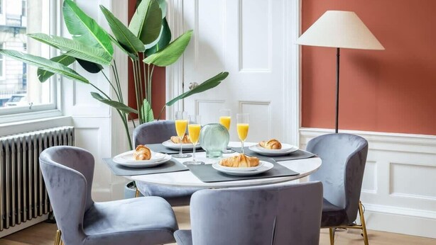 A dining area with a table set for breakfast, including croissants and orange juice, surrounded by chairs. - Ember Suite - City Centre 1 Bed Luxury Apartment (Edinburgh)