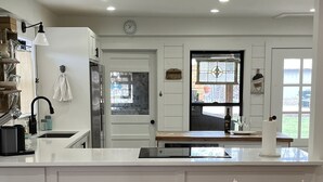 A kitchen with white cabinets, a wooden dining table, and a pink chair. - Centrally located Turn of the Century Beauty! (Kerrville)