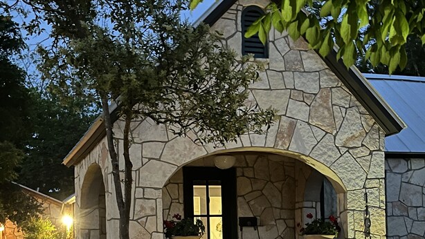 A stone house with a central entrance, two large planters on either side, and a gravel driveway. - Centrally located Turn of the Century Beauty! (Kerrville)