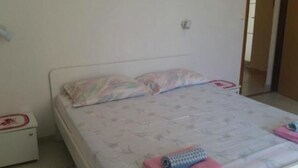 A single-bed room with a white headboard, a bedside table with a red and white object on it, and a bed with a floral-patterned bedspread and pillows. - Apartments Boguvila - One-bedroom Apartment With Terrace - (Supetar)