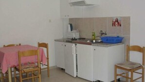 A small kitchen with a white refrigerator, a sink, and a stove. There is a table with a pink tablecloth and wooden chairs. - Apartments Boguvila - One-bedroom Apartment With Terrace - (Supetar)