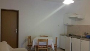 A small, compact room with a kitchenette, a dining table with chairs, and a door. - Apartments Boguvila - One-bedroom Apartment With Terrace - (Supetar)